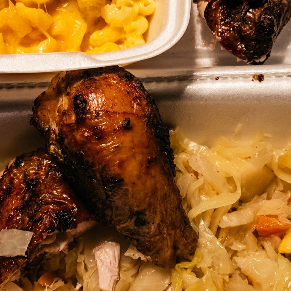 A takeout meal featuring grilled chicken, creamy macaroni and cheese, and stewed cabbage.
