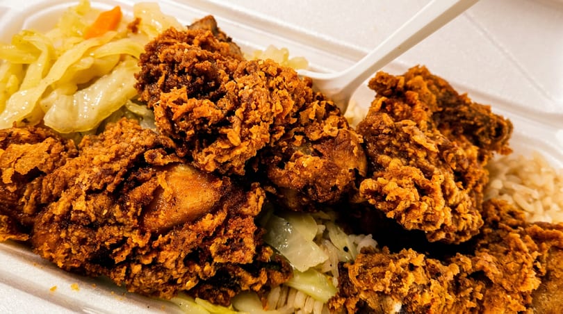 Golden fried chicken pieces, rice, and sautéed cabbage in a white takeout container.